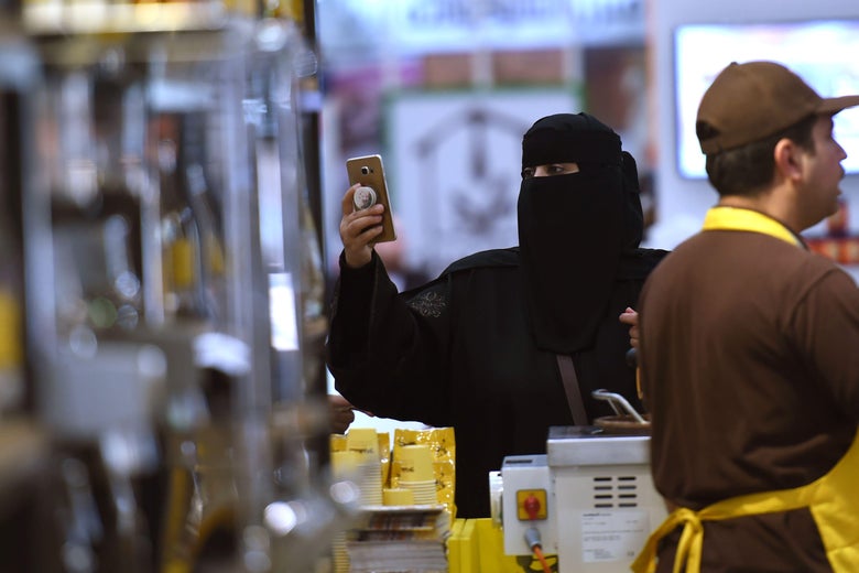 A Saudi woman holds up her cellphone next to a stand at the International Coffee and Chocolate Exhibition.